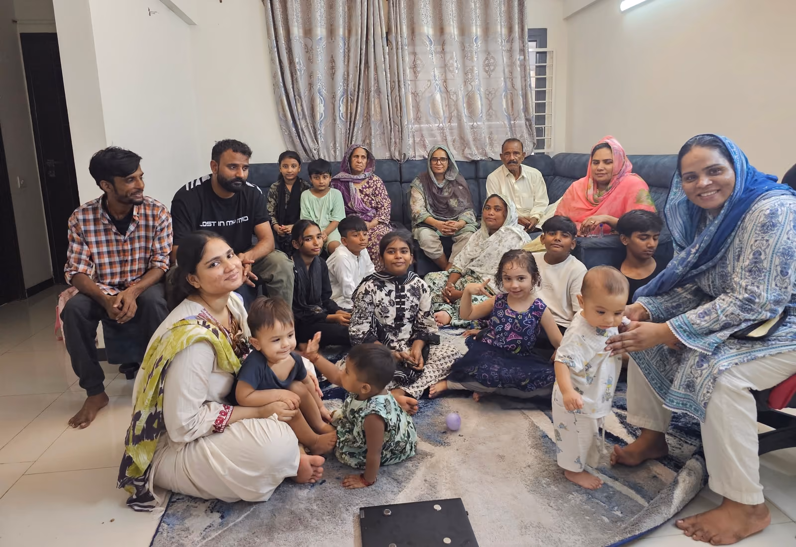 A home fellowship gathered in a living room — three generations together, grandparents on the sofa, parents and children seated on the floor.