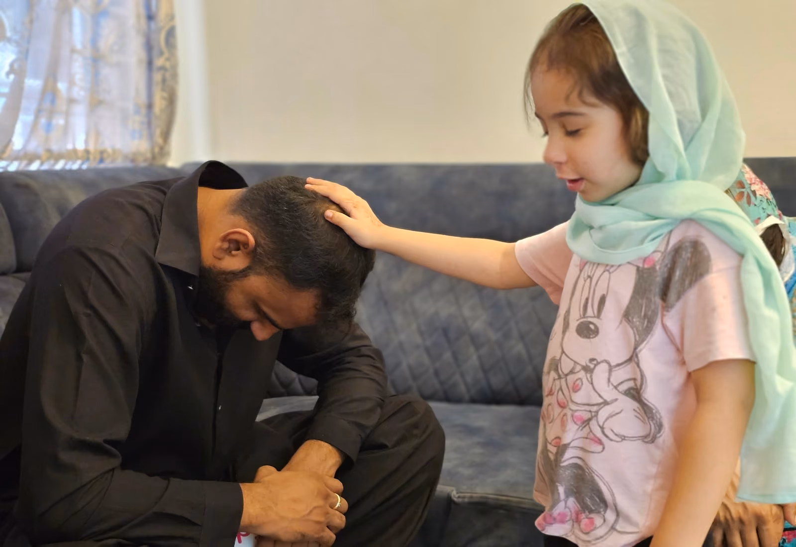 A young girl with her hand on the bowed head of a grown man, praying aloud for him.
